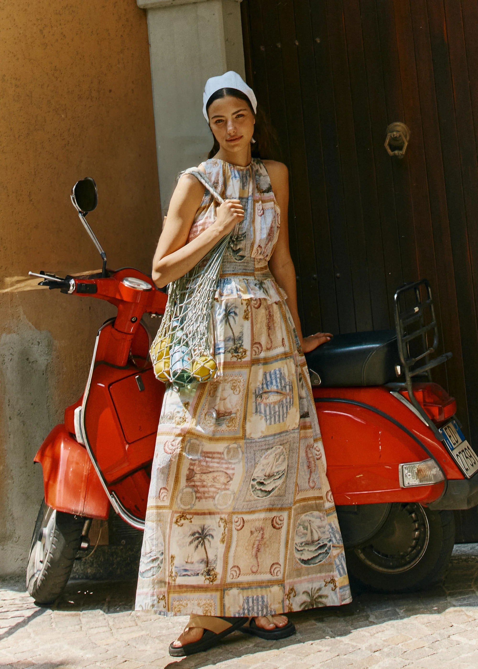 Woman in a patterned dress standing next to a red scooter