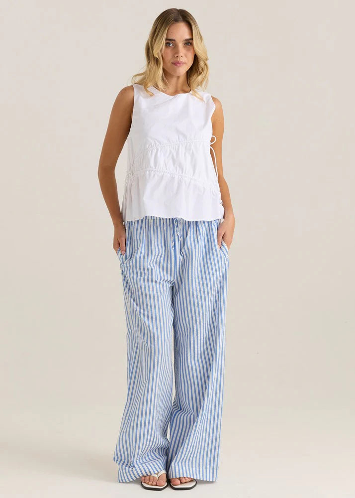 Woman wearing a white sleeveless top and blue striped pants on a beige background