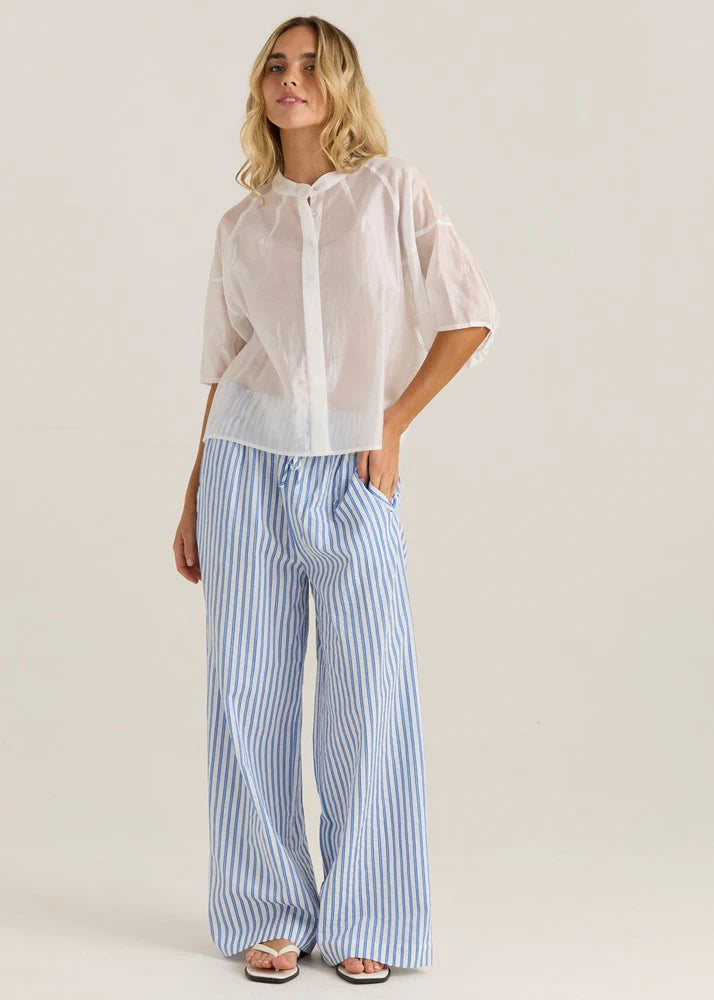 Woman wearing a light pink sheer blouse and blue striped pants on a plain background