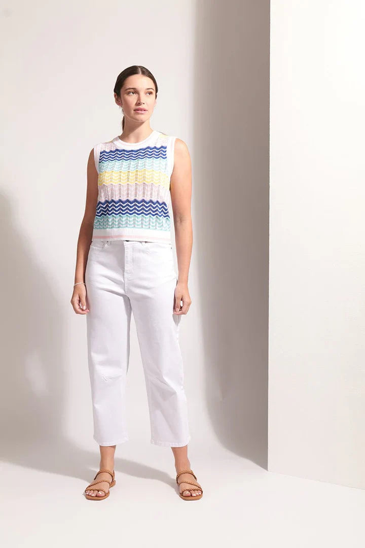 Woman wearing a sleeveless, multicolored zigzag pattern top and white pants on a plain background