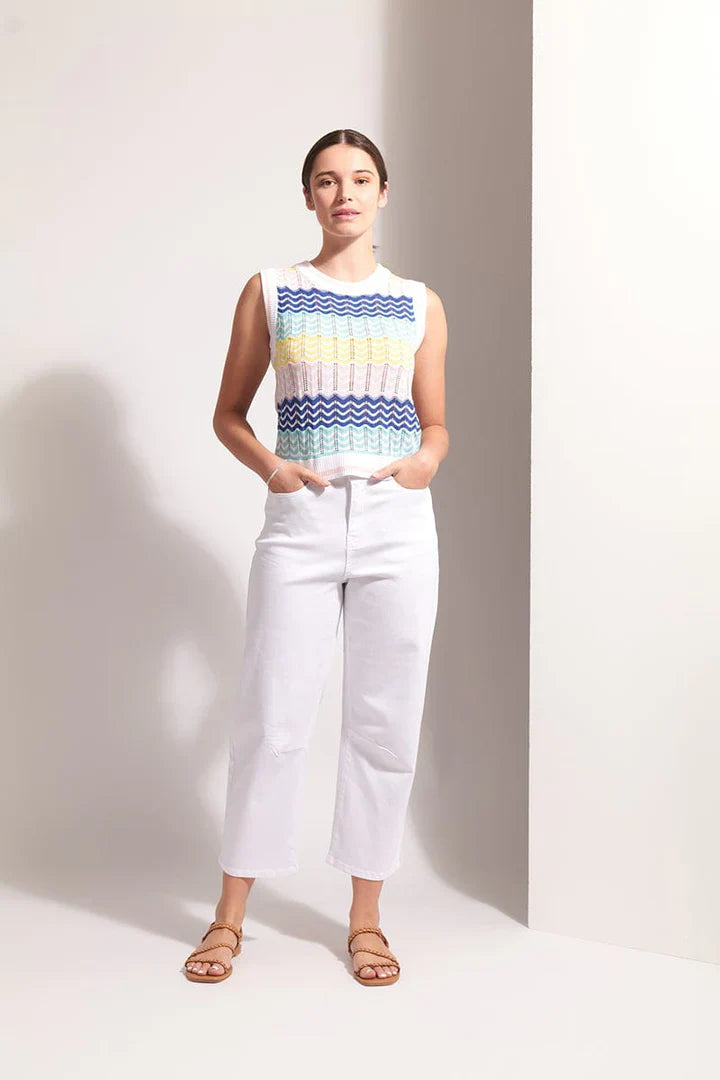 Woman wearing a sleeveless striped top and white pants against a plain background