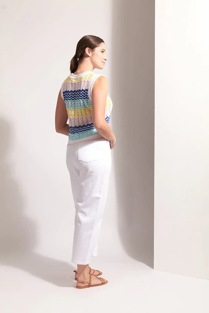 Woman wearing a colorful sleeveless top and white pants against a plain background