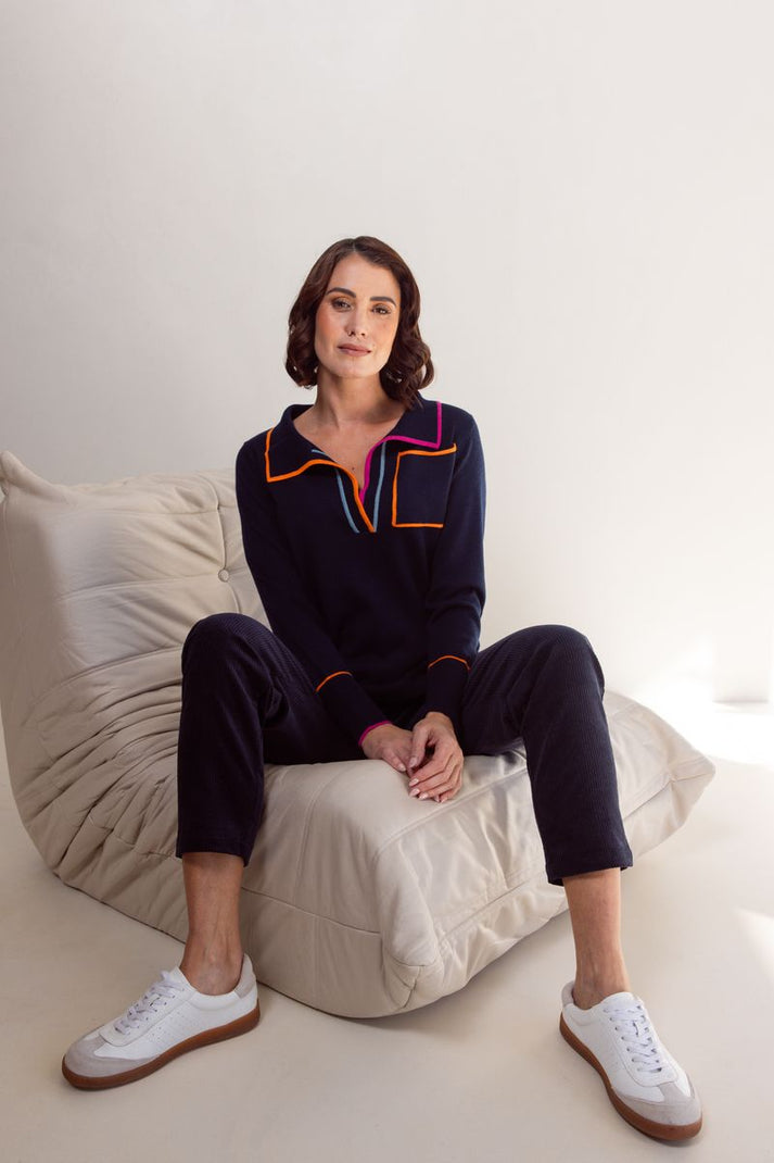 Woman sitting on a white couch wearing a dark blue outfit with colorful accents.