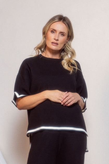 Woman wearing a black outfit with white trim standing against a neutral background