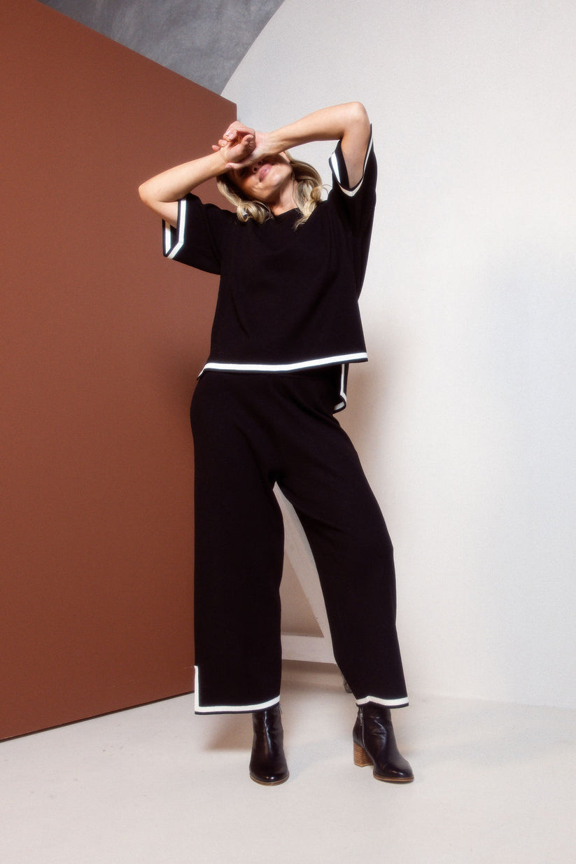 Person wearing a black outfit with white trim against a brown and white wall.