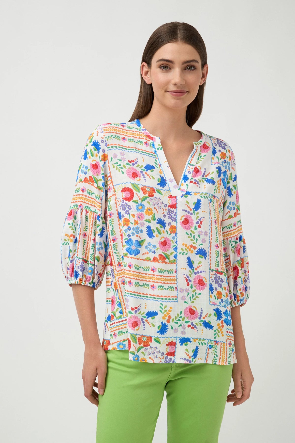 Woman wearing a colorful floral blouse with green pants on a white background