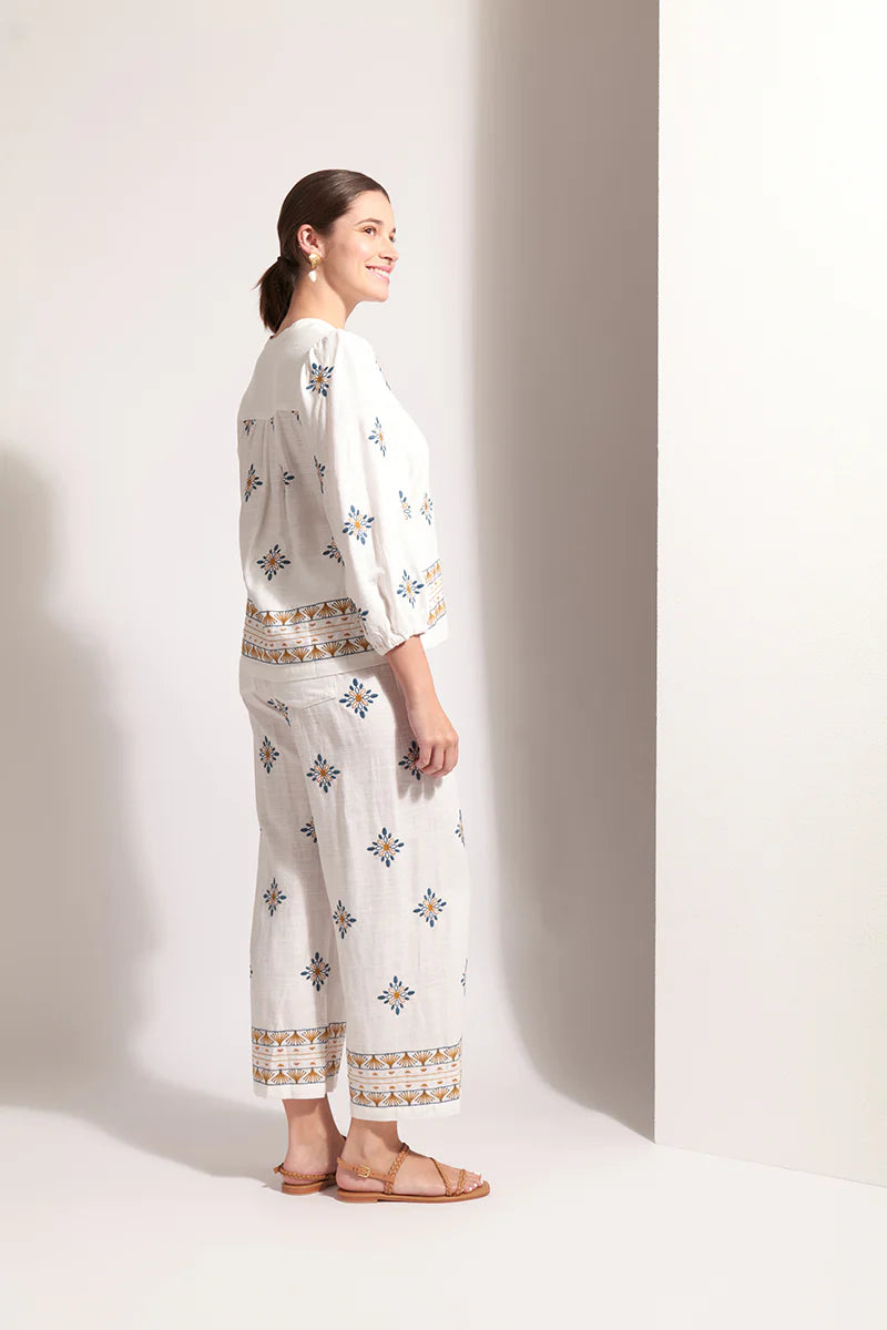 Woman wearing a white outfit with floral patterns on a plain background