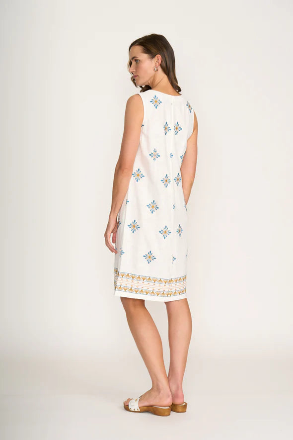 Woman wearing a white dress with blue floral patterns on a plain background