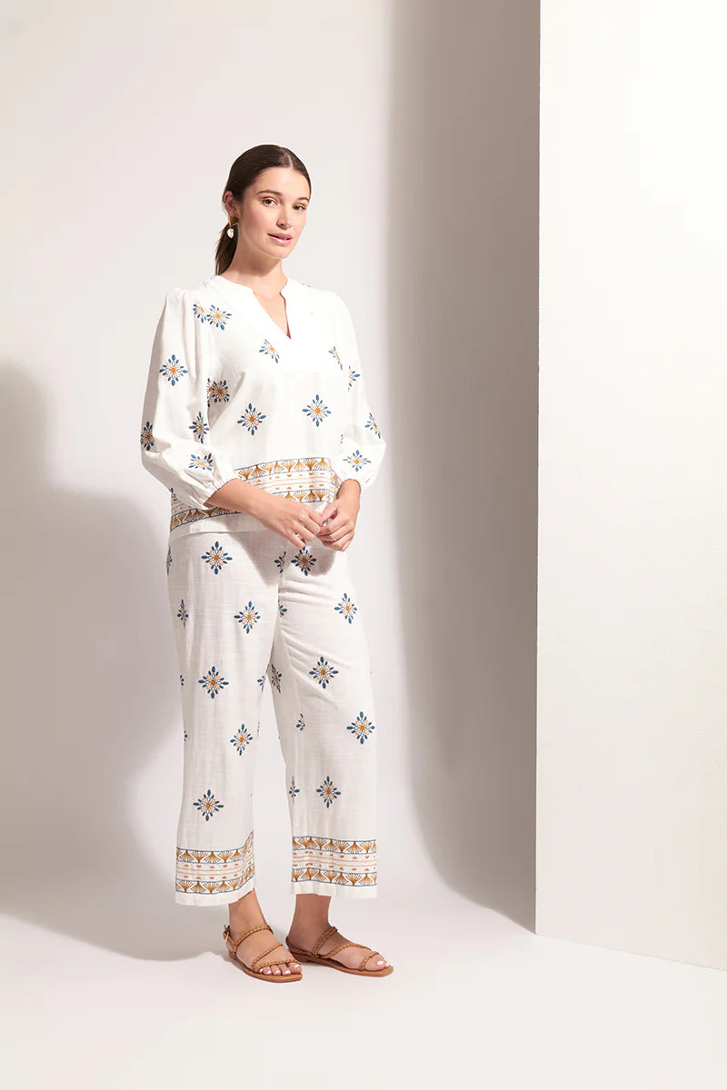 Woman wearing a white outfit with patterned design against a plain background