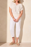 Woman wearing a white lace top and pants with beige sandals on a plain background