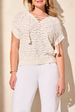 Woman wearing a light-colored lace top and white pants against a beige background