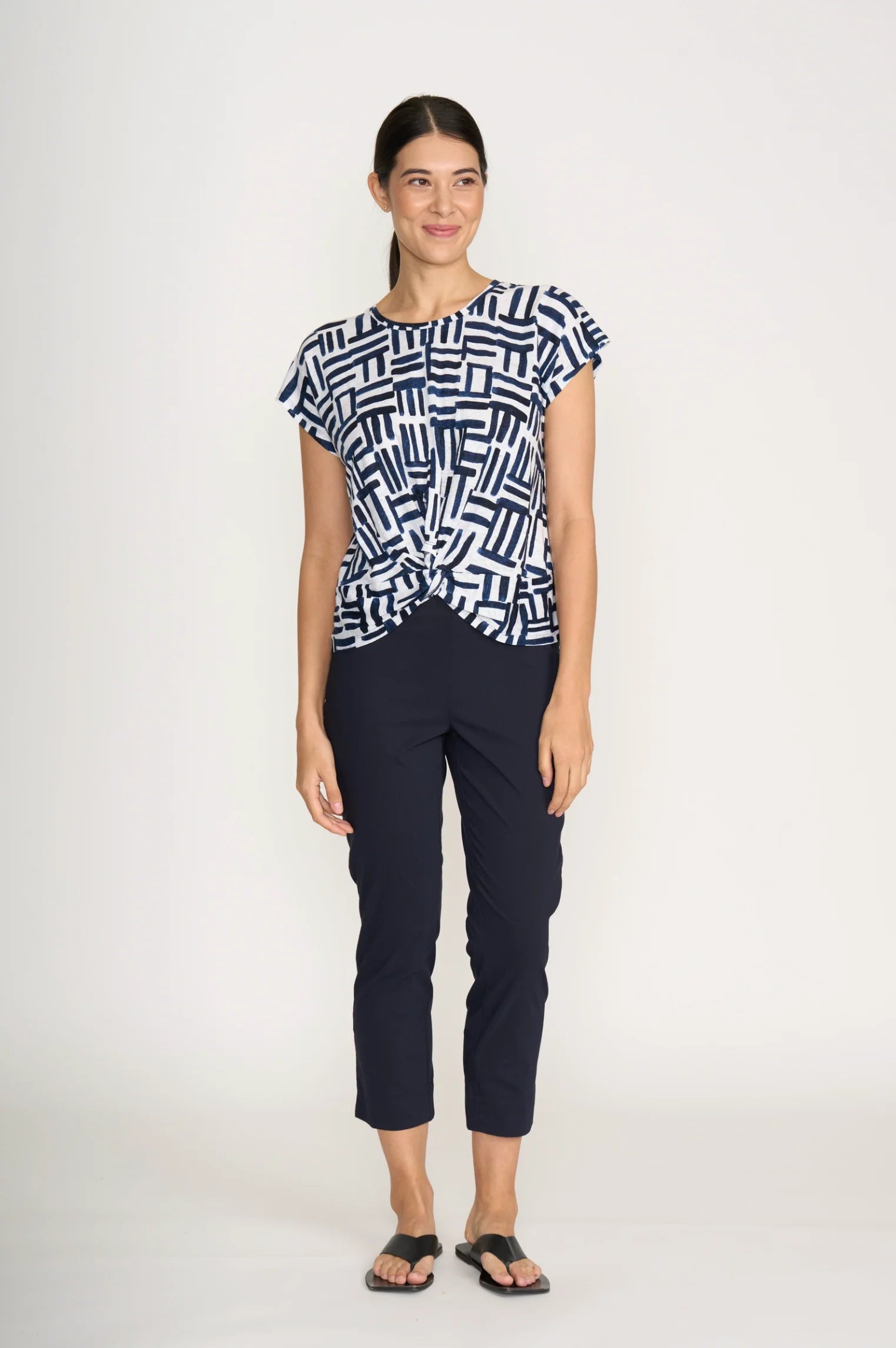 Woman wearing a patterned top and dark pants on a white background