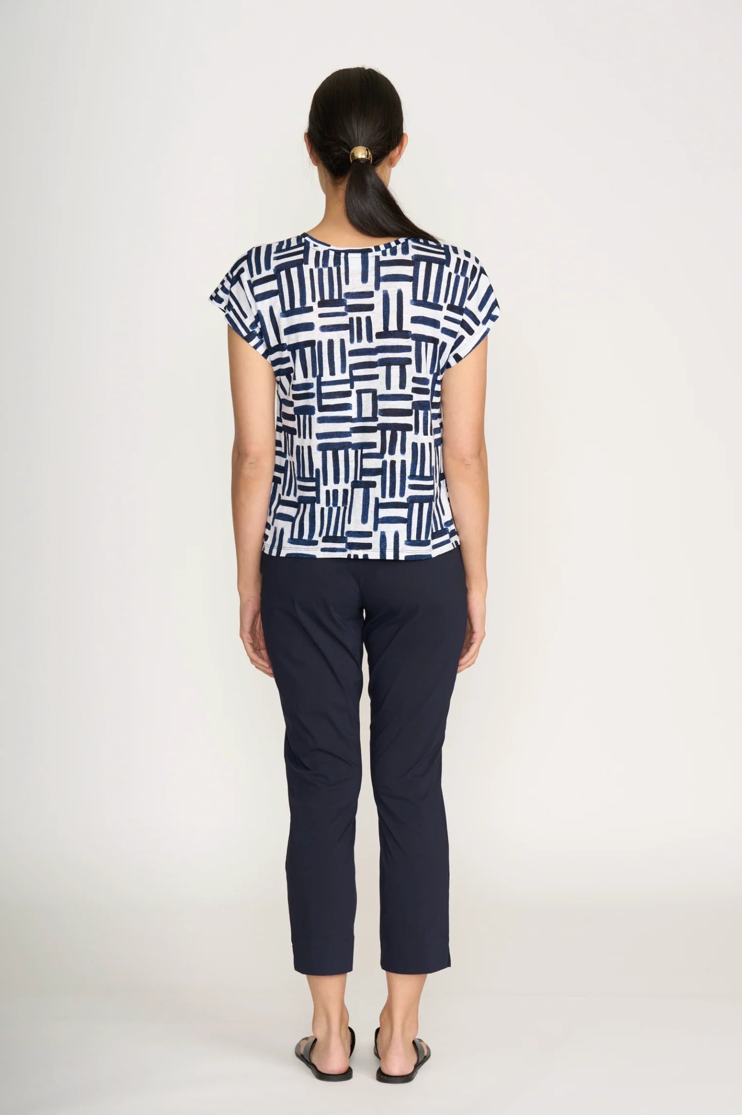 Woman wearing a patterned top and black pants on a white background