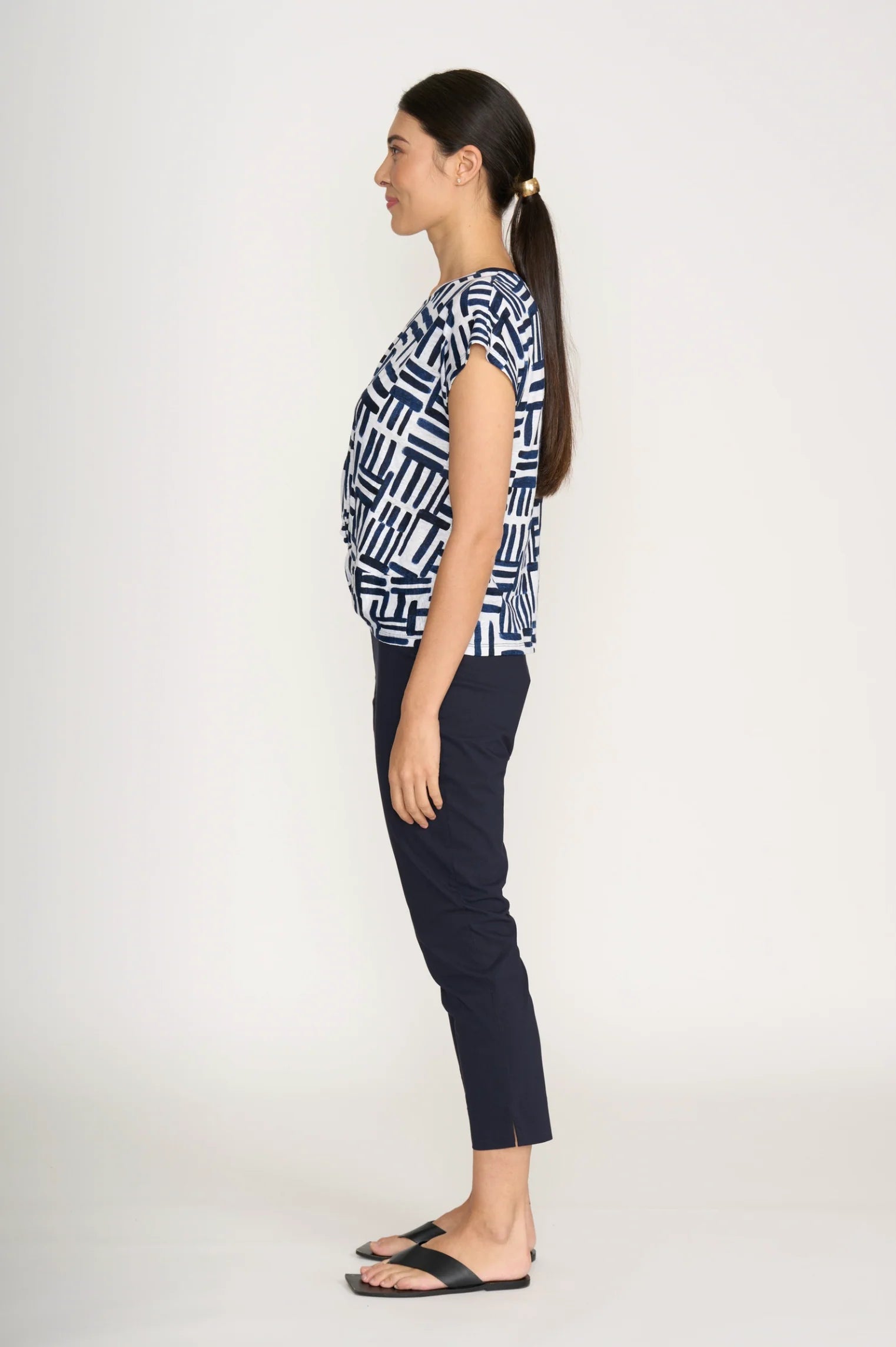 Woman wearing a patterned top and dark pants on a white background