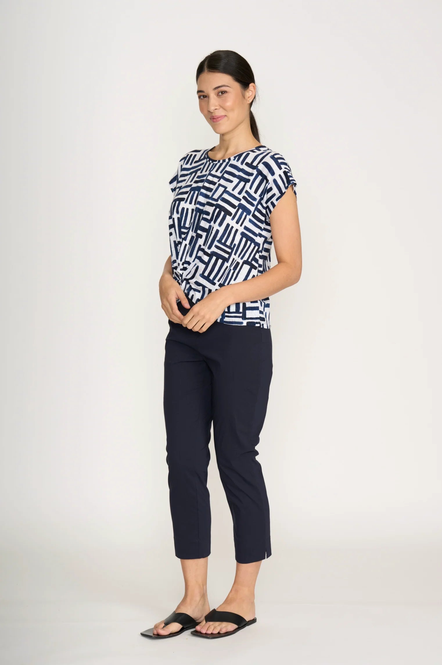 Woman wearing a patterned top and black pants on a white background